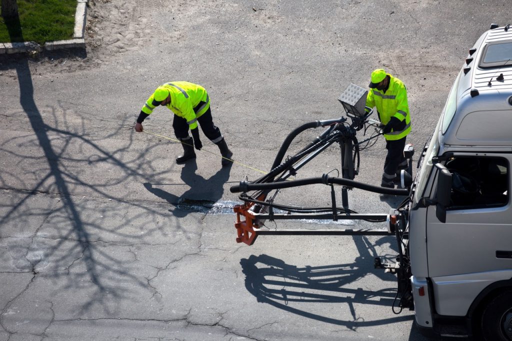 Road surface restoration work. The worker performs on road patcher work on the repair of cracks by filling and sealing with coated by bitumen emulsion and dry aggregate in the asphalt surface.